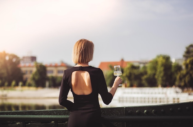 Junge Touristin steht mit einem Glas Weißwein an der Brücke im europäischen Stadtfluss im Hintergrund