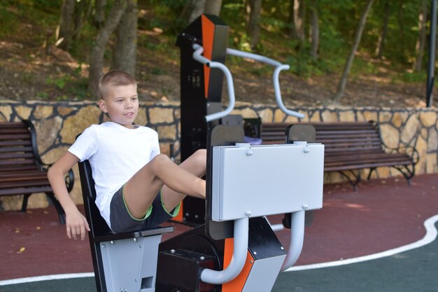 Junge trainiert auf dem Outdoor-Sport-Simulator. Sportkind im Sommer auf Spielplatz.