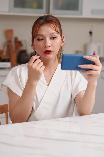 Junge Transgender-Frau benutzt Smartphone als Spiegel beim Auftragen von Lippenstift