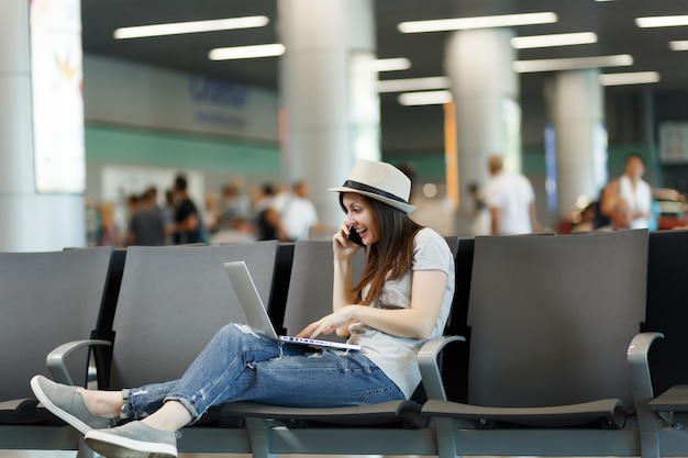 Junge überraschte Reisende Touristenfrau, die am Laptop arbeitet, spricht über Handy-Anruf Freund, der Taxi-Hotel bucht, wartet in der Lobbyhalle am Flughafen