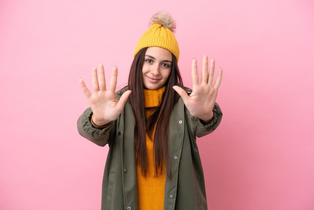 Junge Ukrainerin trägt Winterjacke isoliert auf rosa Hintergrund und zählt zehn mit den Fingern