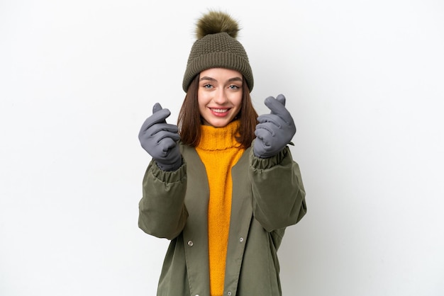Junge Ukrainerin trägt Winterjacke isoliert auf weißem Hintergrund und macht Geldgeste