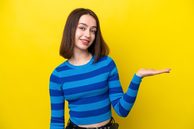 Junge ukrainische Frau isoliert auf gelbem Hintergrund, die eine Idee präsentiert, während sie lächelnd in Richtung schaut