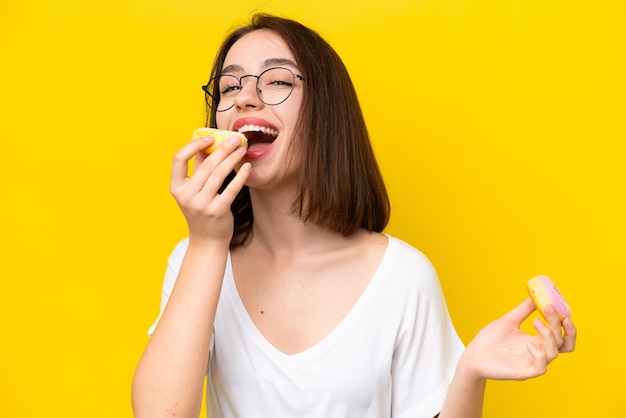 Junge ukrainische Frau isoliert auf gelbem Hintergrund, die einen Donut isst