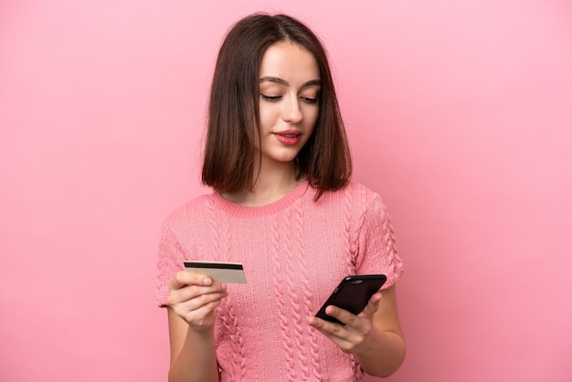 Junge ukrainische Frau isoliert auf rosafarbenem Hintergrund, die mit dem Handy mit einer Kreditkarte kauft