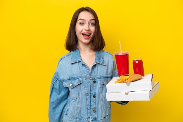 Junge ukrainische Frau mit Fast Food isoliert auf gelbem Hintergrund mit überraschendem Gesichtsausdruck