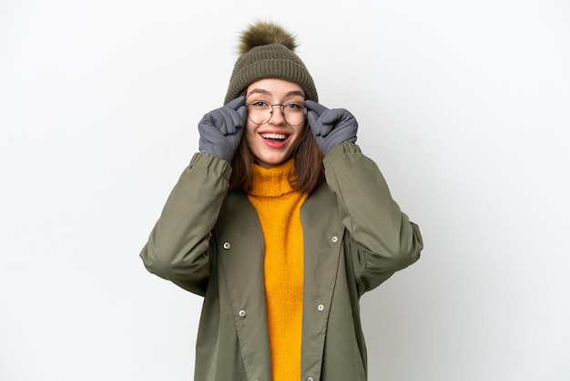 Junge ukrainische frau trägt winterjacke isoliert auf weißem hintergrund mit brille und überrascht