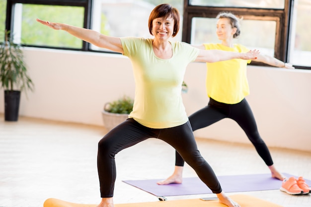 Junge und ältere Frauen in Sportkleidung, die zu Hause oder im Fitnessstudio zusammen Yoga machen