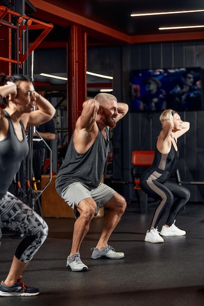 Junge und aktive Menschen beim Gruppensporttraining wärmen sich gemeinsam auf und machen Übungen für die Armstreckung Menschen trainieren in einem geräumigen, hellen Fitnessstudio Konzept von Sport und gesundem Lebensstil