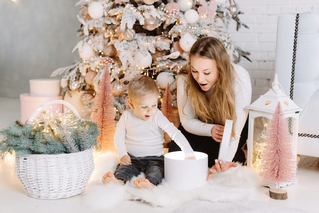 Junge und blonde hübsche Frau genießen Weihnachtszeit, die Geschenke unter Weihnachtsbaum öffnet