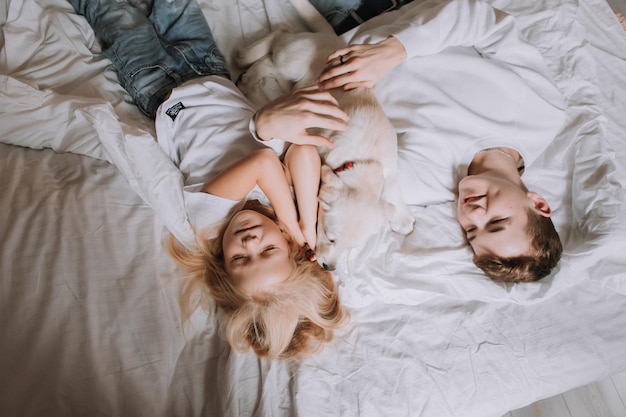 Junge und ein Mädchen in weißen T-Shirts, Bruder und Schwester liegen mit einem Hund in einem Bett aus weißer Bettwäsche. Ansicht von oben. Lieblingstier. Platz für Texte. Foto in hoher Qualität