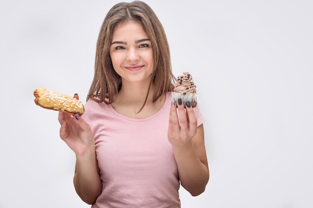 Junge und fröhliche Frau halten gelben Eclair und Schokoladencupcake in den Händen