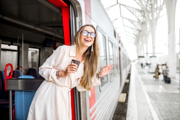 Junge und glückliche Frau, die das Gesicht aus der Zugtür zieht und nach jemandem am Bahnhof sucht