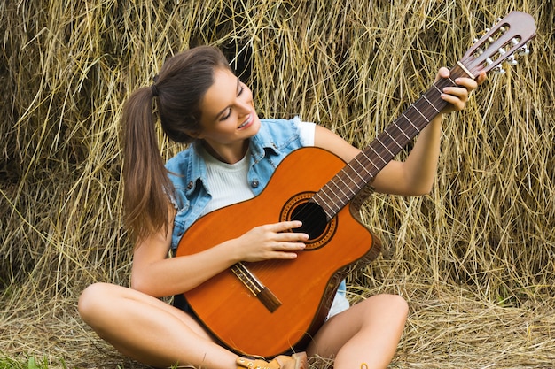 Junge und glückliche Frau, die Gitarre im Dorf spielt
