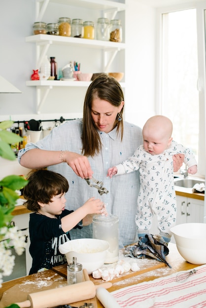 Junge und glückliche Mutter mit ihren Kindern in der Küche kochen Keksteig oder Kuchen