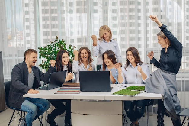 Junge und glückliche Partner im Büro, die die gute Nachricht erfahren haben, sitzen am selben Tisch und lächeln im Büro. Arbeitskonzept