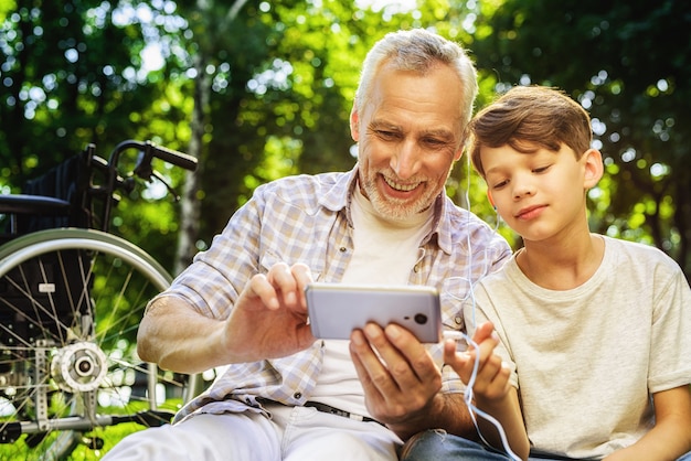 Junge und Großvater halten Smartphone. Familienpicknick.