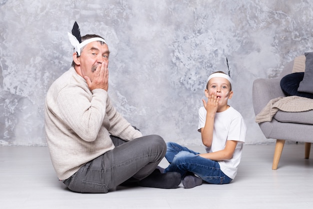 Junge und Großvater spielen Indianer auf einer grauen Wandwand. Älterer Mann und Enkel spielen Injun im Wohnzimmer. Familie zusammen