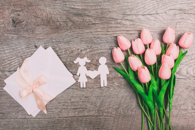 Junge und Mädchen aus Papier geschnitten, und in der Mitte ist ein Herz auf einem hölzernen Hintergrund. Valentinstag