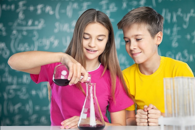 Junge und Mädchen, die chemische Experimente durchführen. Flüssigkeit in Becher gießen