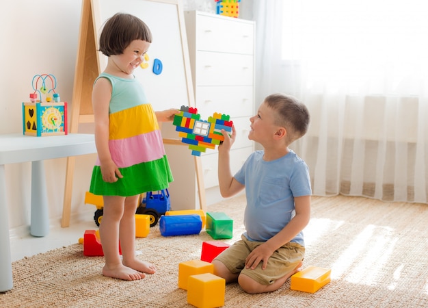 Junge und Mädchen halten Herz aus Plastikblöcken. Bruder und Schwester haben Spaß zusammen zu spielen