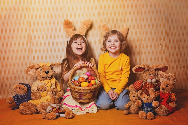 Junge und Mädchen mit den Hasenohren, die um viele Stroh- und Plüschhasen, Weinleseart sitzen.