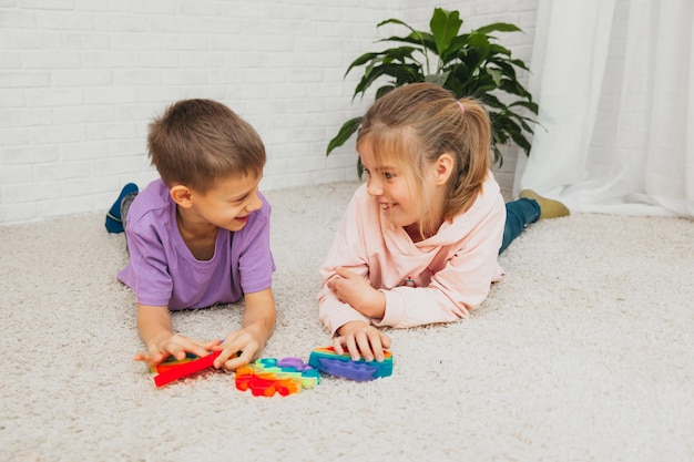 Junge und Mädchen sitzen auf dem Boden und spielen mit Silikonspielzeug, Antistress. Pop ist ein sensorisches Spielzeug. Stress abbauen.