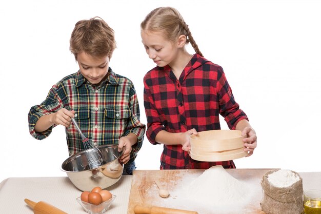 Junge und Mädchen tun Teig zum Backen, Bruder und Schwester, Junge Schlagsahne, Mädchen, das Mehl sieben, auf weißem Hintergrund, isolieren