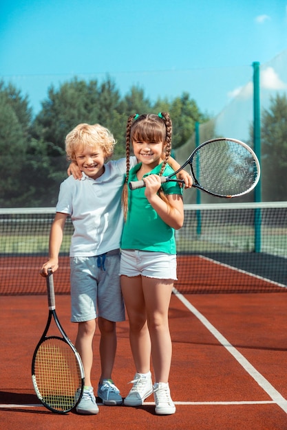 Junge und Mädchen umarmen sich, während sie sich nach dem Tennisspielen glücklich fühlen