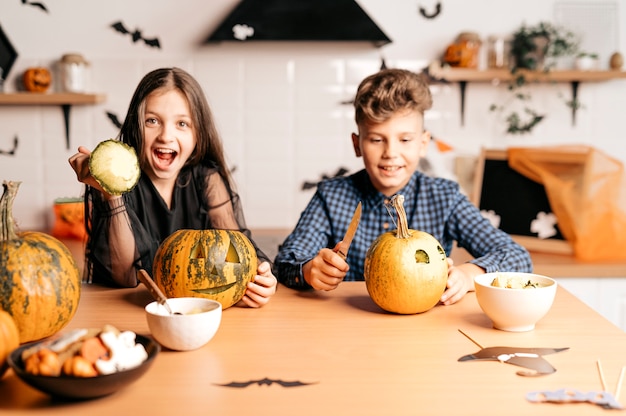 Junge und Mädchen zu Hause in der Küche sitzen mit Kürbisspiel und lachen Halloween-Konzept