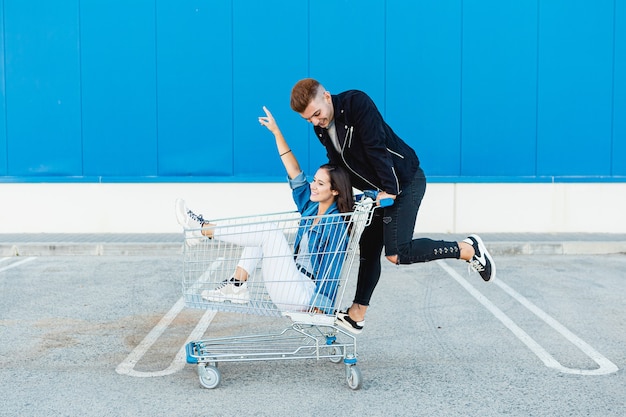 Junge und Paar, die Spaß in einem Einkaufswagen im blauen Hintergrund haben.