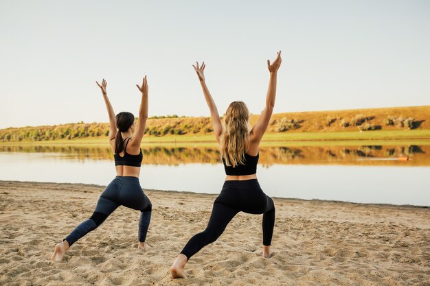 Junge und schöne Freundin machen Yoga am Sandstrand.