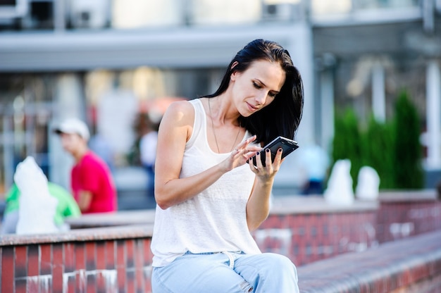 Junge und schöne moderne Geschäftsfrau wirft im Freien mit intelligentem Telefon auf.