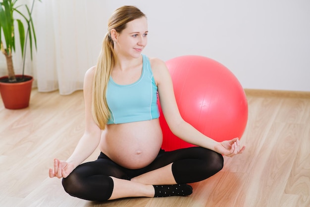 Junge und schwangere Frau im Sportanzug, die zu Hause Übungen mit einem großen Ball macht