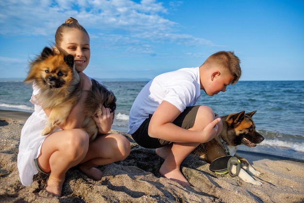 Junge und seine Schwester in leichter Kleidung spazieren und entspannen sich mit Hunden Pomeranian und Akita Inu am Strand entlang des Schwarzen Meeres