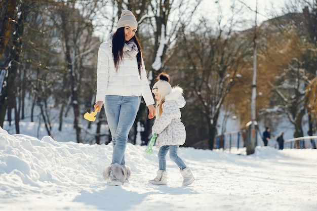 Junge und stilvolle Mutter, die mit ihrer kleinen netten Tochter im Winterschneepark spielt