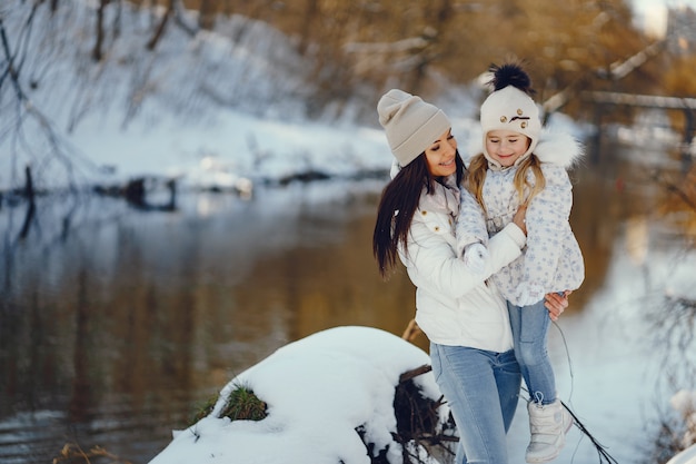 Junge und stilvolle Mutter, die mit ihrer kleinen netten Tochter im Winterschneepark spielt