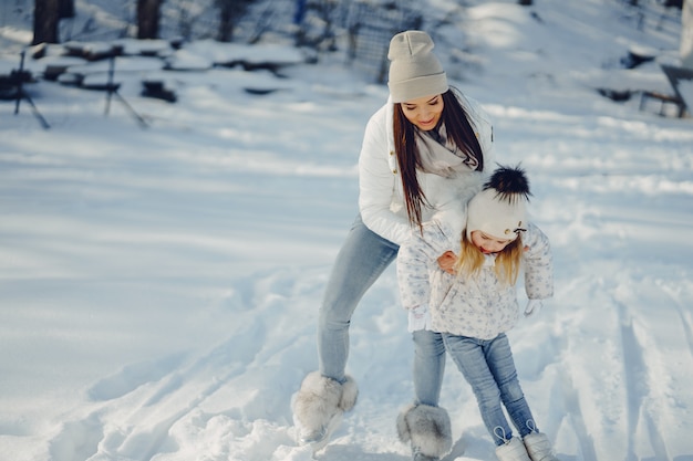 Junge und stilvolle Mutter, die mit ihrer kleinen netten Tochter im Winterschneepark spielt