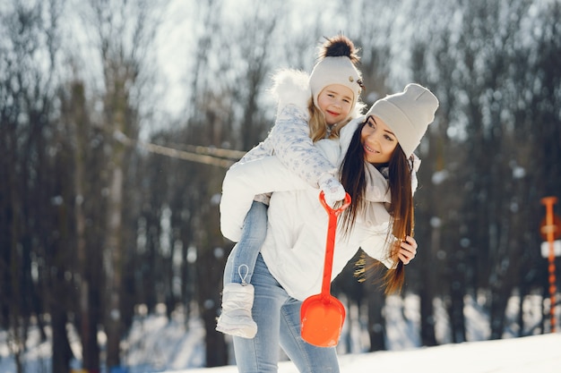 Junge und stilvolle Mutter, die mit ihrer kleinen netten Tochter im Winterschneepark spielt