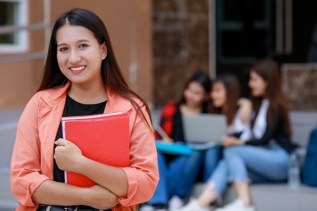 Junge und süße asiatische College-Studenten, die Bücher halten, posieren für die Kamera.