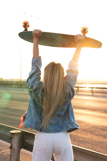 Junge und unbeschwerte Frau mit einem Longboard auf einer Brücke bei Sonnenuntergang