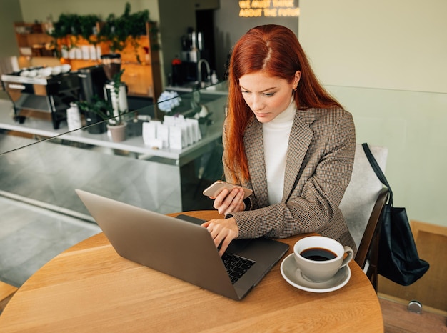 Junge Unternehmerin, die in einem Café arbeitet Frau mit Ingwerhaar, die auf einem Laptop tippt