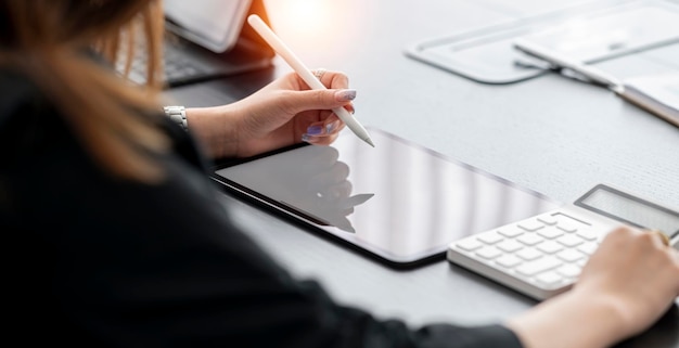 Junge Unternehmerin mit digitalem Tablet und Taschenrechner im Büro