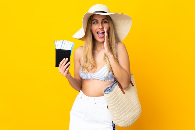 Junge uruguayische blonde Frau im Badeanzug, die einen Reisepass über isoliertem gelbem Hintergrund hält und mit weit geöffnetem Mund schreit
