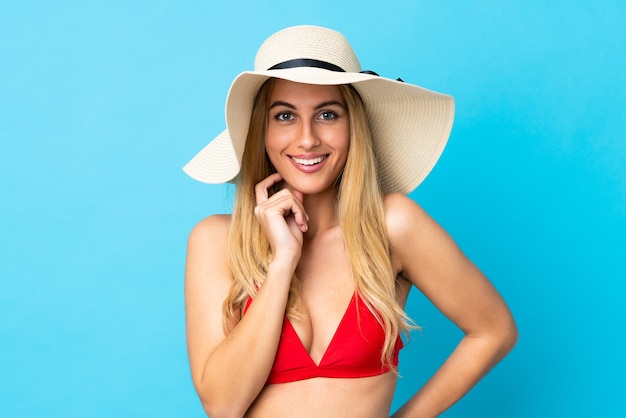 Junge uruguayische blonde Frau über isoliertem blauem Hintergrund glücklich im Badeanzug in den Sommerferien