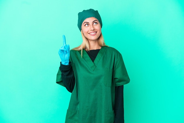 Junge uruguayische Chirurgin in grüner Uniform isoliert auf blauem Hintergrund nach oben zeigend und überrascht