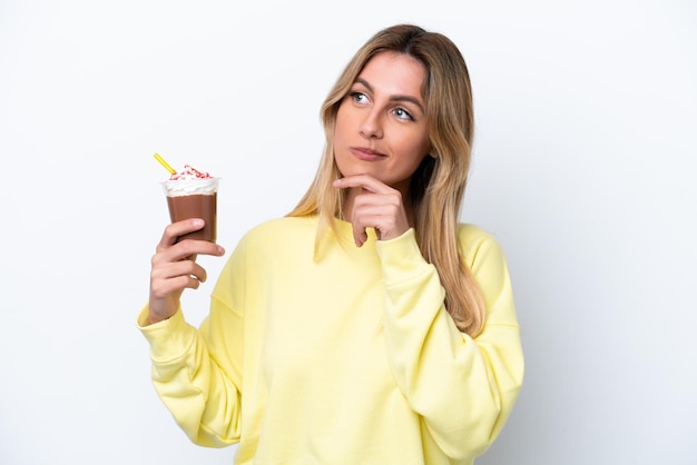 Junge uruguayische Frau, die Frappuccino isoliert auf weißem Hintergrund hält, hat Zweifel und denkt nach
