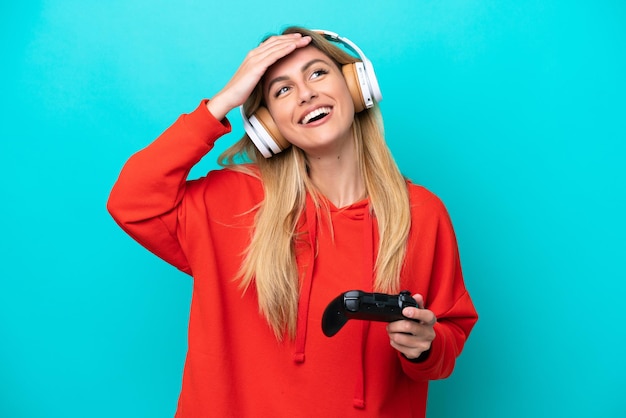 Junge uruguayische Frau, die mit einem Videospiel-Controller spielt, isoliert auf Blau, lächelt viel