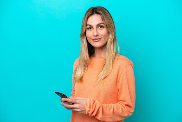 Junge uruguayische Frau isoliert auf blauem Hintergrund, die eine Nachricht mit dem Handy sendet