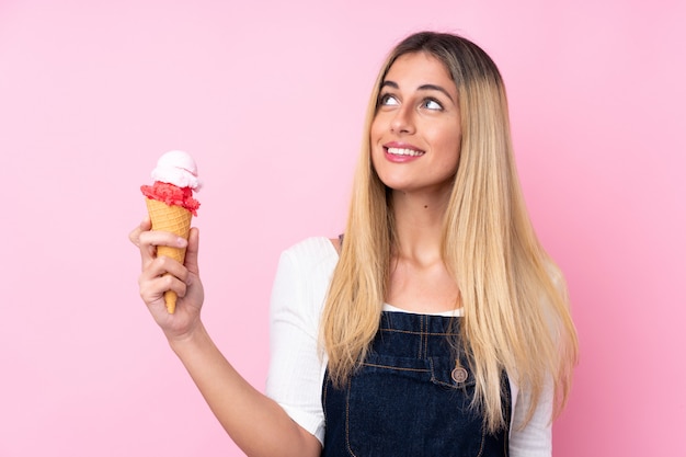 Junge uruguayische Frau mit einem Kornett-Eis über der isolierten rosa Wand, die beim Lächeln nach oben schaut